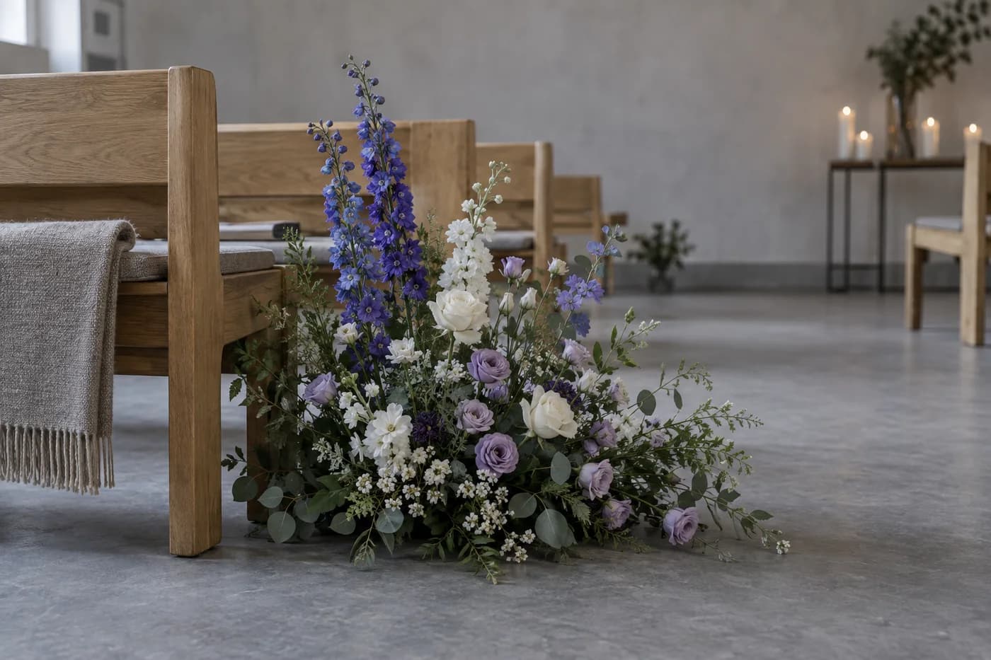 Lilla og hvite begravelsesblomster ved en enkel trebenk i et seremonirom